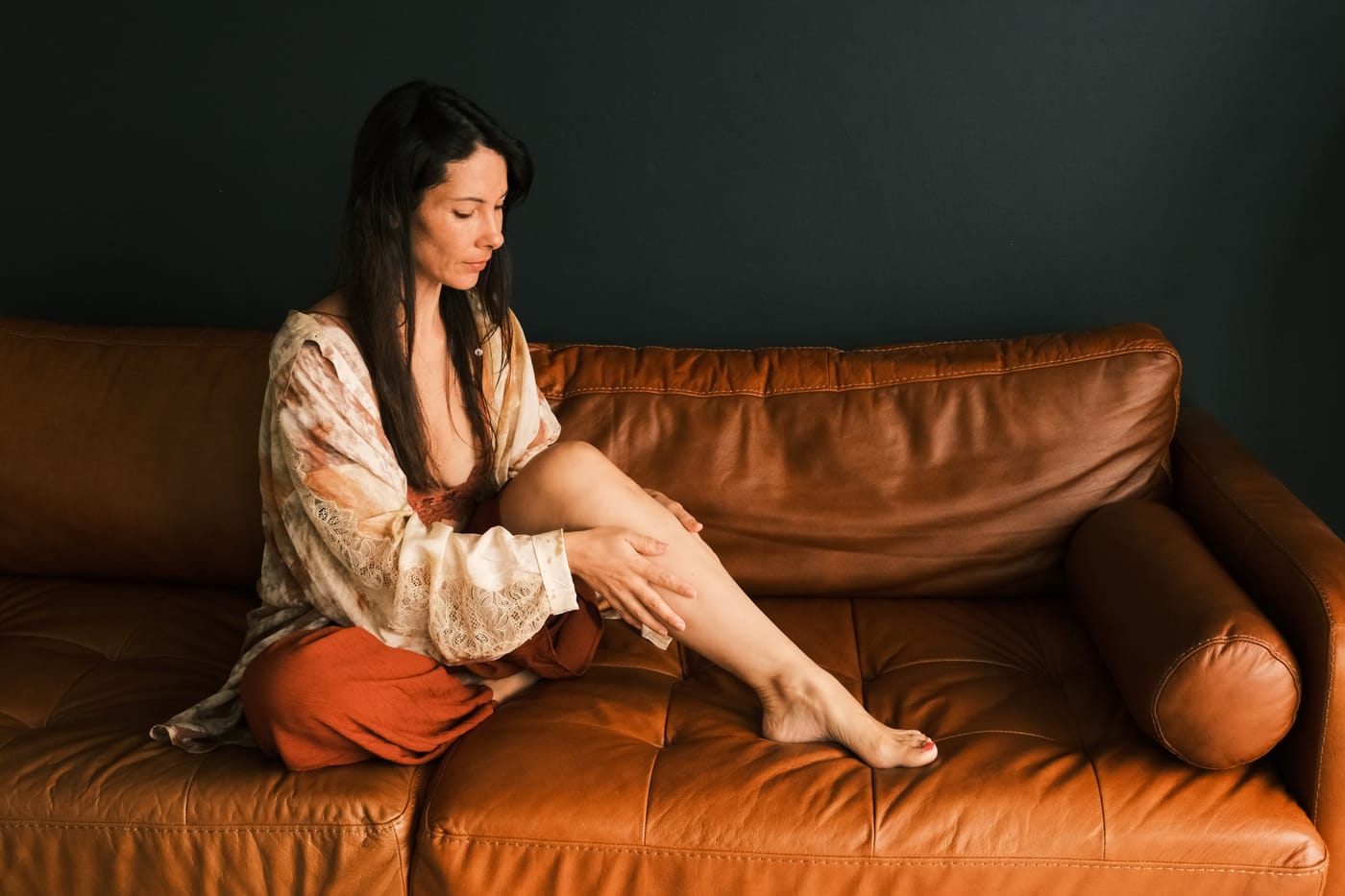 Chloé assise sur un canapé, pratiquant un automassage de la jambe