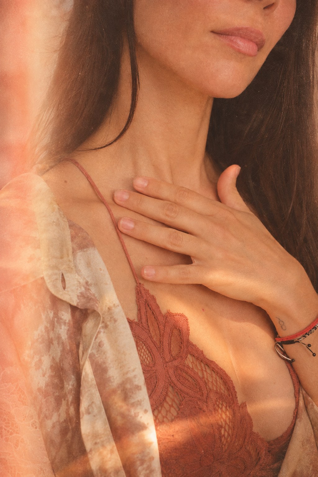 Une femme pose doucement la main sur sa clavicule, dans une lumière chaude